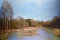 Long shot of a landscape with a small calm river that flows calmly in the winter in front of barren trees and dry grass Royalty Free Stock Photo