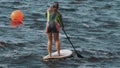 Long shot of women in full swimsuit shaky tryes to ride a surfboard using paddle