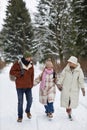 Long shot of young family in winterwear walking down forest road Royalty Free Stock Photo