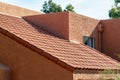 Long slanted adobe style roof with red tiles and orange stucco exterior with back and front yard trees in a neighborhood