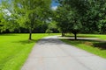 A long smooth curved street in the park surrounded by lush green grass and lush green trees with blue sky and clouds Royalty Free Stock Photo