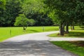 A long smooth curved street in the park surrounded by lush green grass and lush green trees with blue sky and clouds Royalty Free Stock Photo