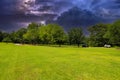 A long smooth winding road surrounded by lush green grass and lush green trees with powerful storm clouds and lightning Royalty Free Stock Photo