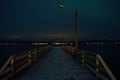 Long snowy wooden pier with faint aurora borealis over mountain and fjord