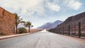 Long straight road with desert hills in distance, brick wall and iron fence on sides. Scenery at the entrance to Wadi Rum Royalty Free Stock Photo