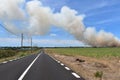 Long straight road through open countryside with a fire who just burst into a field Royalty Free Stock Photo