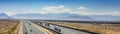 A long and straight stretch of highway with cars and trucks traveling in both directions, surrounded by open landscapes and a