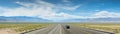 A long and straight stretch of highway with cars and trucks traveling in both directions, surrounded by open landscapes and a