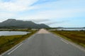 Long strait road with ocean water on sides and mighty mountains in summer