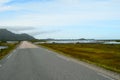Long strait road with ocean water on sides and mighty mountains in summer