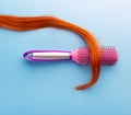 Long strand of hair with hair comb on blue background isolated, top view. Hairdresser composition with hairbrush combing curl of