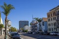 A long street lined with parked cars, office buildings, apartments, lush green palm trees and shops and cars driving Royalty Free Stock Photo