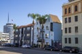 A long street lined with parked cars, office buildings, apartments, lush green palm trees and shops and cars driving Royalty Free Stock Photo