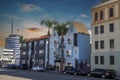 A long street lined with parked cars, office buildings, apartments, lush green palm trees and shops and cars driving Royalty Free Stock Photo