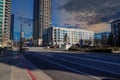 A long street with office buildings, skyscrapers and tall black light posts and cars on the street and bare winter trees