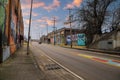 A long street with tall telephone poles and colorful wall murals and bare winter trees and tall curved light posts with blue sky