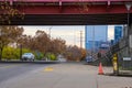 A long street with a yellow line and cars and trucks parked along the street underneath a red metal bridge