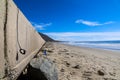A long stretch of a concrete bridge at beach with RVs parked along the street and rocks along the beach with silky sand