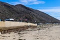 A long stretch of a concrete bridge at beach with RVs parked along the street and rocks along the beach with silky sand