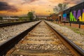 A long stretch of metal and wooden railroad tracks surrounded by gravel, red brick buildings and lush green trees