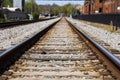 A long stretch of metal and wooden railroad tracks surrounded by gravel, red brick buildings and lush green trees Royalty Free Stock Photo