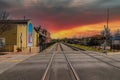 A long stretch of railroad tracks covered in gravel with a black metal fence and buildings along the tracks and blue sky