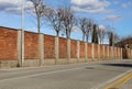 Long surrounding brick wall with pole and concrete columns at the road side. Bare trees, street lamp and sky on behind. Royalty Free Stock Photo