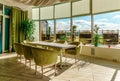 A long table with armchairs in Pastel restaurant awaits guests. Ambient sunlight interior view with a large window