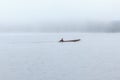 Long tail boat with a fisherman inside on river with foggy background.