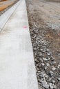 Long view down freshly extruded concrete curb beside road bed under construction