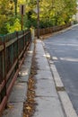 Long view of a very narrow sidewalk bordered by street and rusted wrought iron fencing, trees with leaves Royalty Free Stock Photo