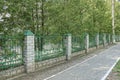 A long wall of green metal and white brick fence on the street