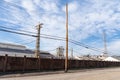 Long wall between street and industrial steel mill, power lines, blue sky with clouds