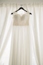Long white dress of the bride with a lace corset on a black hanger against a background of white curtains. Royalty Free Stock Photo