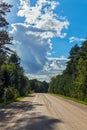 A long, wide dirt road running between tall trees and bushes growing on the roadside against a background of dense white Royalty Free Stock Photo