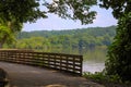 A long winding boardwalk along the river with a wooden rail along the sides with vast still river water, lush green trees