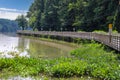 A long winding boardwalk along the river with a wooden rail along the sides with vast still river water, lush green trees Royalty Free Stock Photo