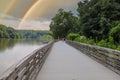 A long winding boardwalk along the river with a wooden rail along the sides with vast still river water, lush green trees Royalty Free Stock Photo