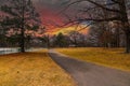 A long winding footpath along side of a green lake in the park surrounded by yellow winter grass, bare winter trees Royalty Free Stock Photo