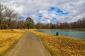 A long winding footpath in the park surrounded by yellow winter grass, bare winter trees, lush green trees, blue sky Royalty Free Stock Photo