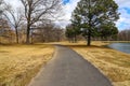 A long winding footpath in the park surrounded by yellow winter grass, bare winter trees, lush green trees, blue sky Royalty Free Stock Photo