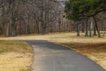 A long winding footpath in the park surrounded by yellow winter grass, bare winter trees, lush green trees, blue sky Royalty Free Stock Photo