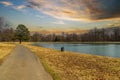 A long winding footpath in the park surrounded by yellow winter grass, bare winter trees, lush green trees, blue sky Royalty Free Stock Photo