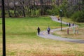 A long winding footpath with a yellow line in the park surrounded by lush green grass, tall black light posts with people walking