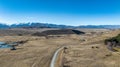 Long winding narrow gravel road across rural farming countryside towards the snow capped Southern alps mountain range Royalty Free Stock Photo