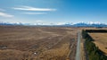 Long straight narrow gravel road across rural agricultural countryside towards the snow capped Southern alps mountain range Royalty Free Stock Photo