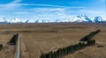 Long straight narrow gravel road across rural agricultural countryside towards the snow capped Southern alps mountain range Royalty Free Stock Photo