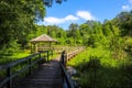 A long winding wooden bridge over silky brown water in a marsh with a wooden pergola surrounded by lush green trees, plants Royalty Free Stock Photo