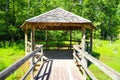 A long winding wooden bridge over silky brown water in a marsh with a wooden pergola surrounded by lush green trees, plants Royalty Free Stock Photo