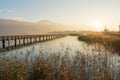 Long wooden boardwalk pier over water in golden evening light with a mountain landscape silhouette in the background and golden ma Royalty Free Stock Photo